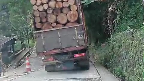 a truck loaded with wood passes through a narrow road, the truck tilts