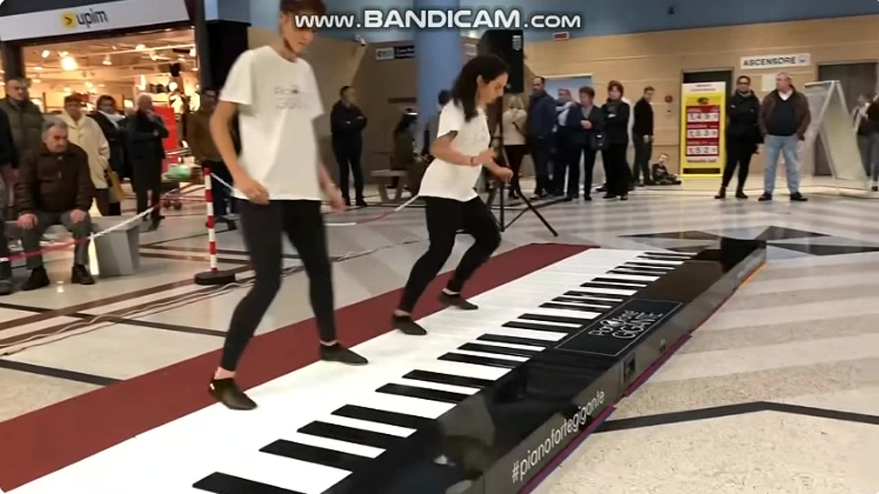 two girls play a very big piano together