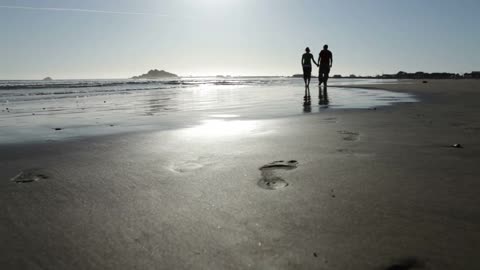 Couple walking, holding hands on sandy beach