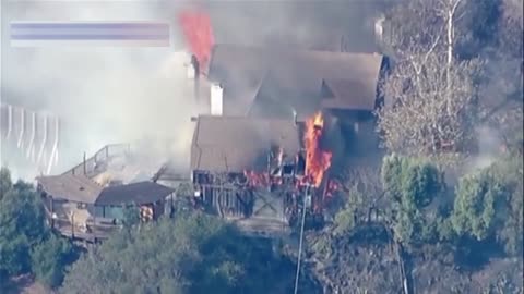 Aerial footage shows helicopters dropping water on a burning LA home