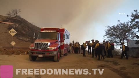 Wall of flames burning near houses in Brentwood. Firefighters huddle before heading to battle