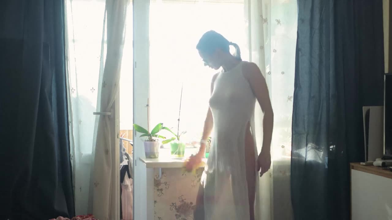 Transparent door cleaning and watering houseplants with model in a dress