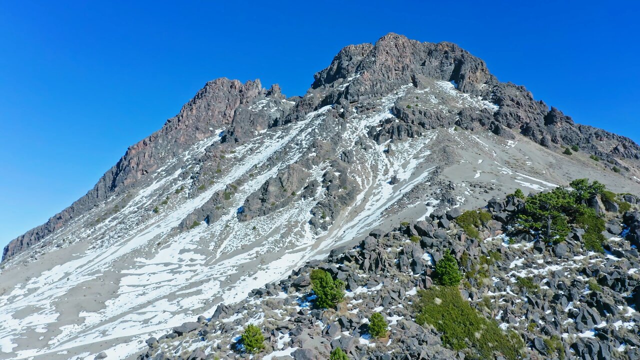 Flying over a monumental rocky mountain with visible snow and small greenery patches