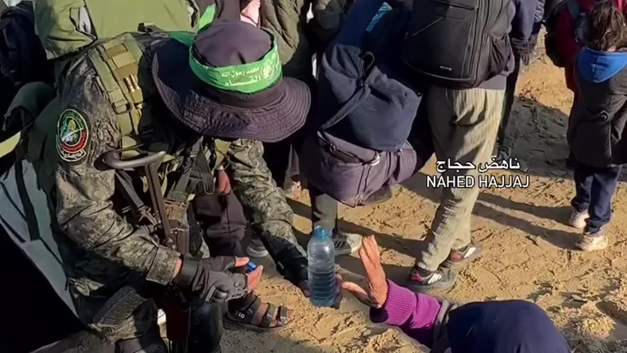 A member of the Al-Qassam Brigades offers a bottle of water to an elderly woman