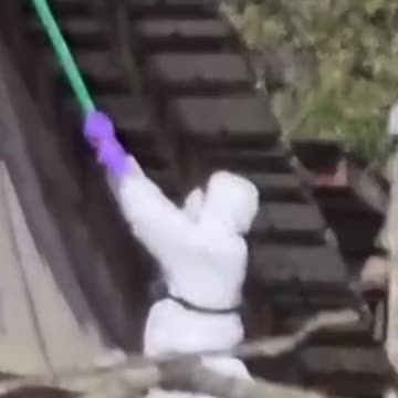 CFIA agent climbs a ladder and uses a pole with tape on the end to cover a security camera