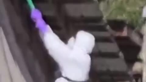 CFIA agent climbs a ladder and uses a pole with tape on the end to cover a security camera