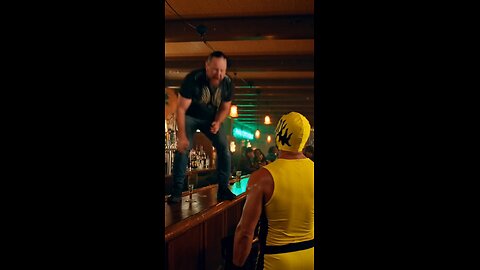 Russell Blade jumps off a bartender's table and clothes lines a yellow mask wrestler at a bar.