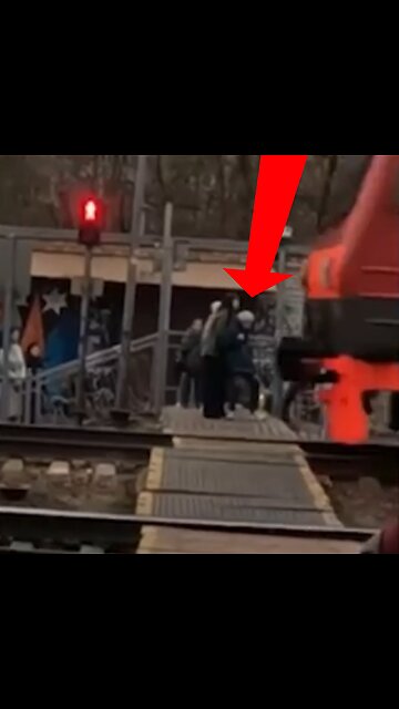 Una joven aparta a una anciana de la ferrovía momentos antes de la llegada de un tren