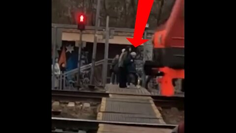 Una joven aparta a una anciana de la ferrovía momentos antes de la llegada de un tren