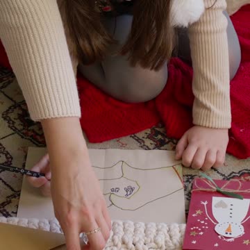 A little girl positioned comfortably on the floor receives help from an adult.