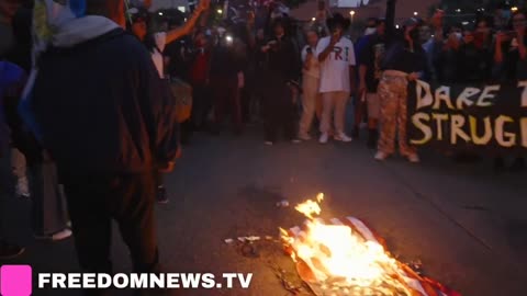 Rioters in Los Angeles are spitting on and setting fire to USA flags while chanting “Fuck Trump.”