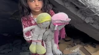 A girl holding the dolls of her friends who were martyred in an Israeli airstrike.