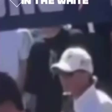 Guys in White and Black standing behind Charlie making what appears to be hand signals.