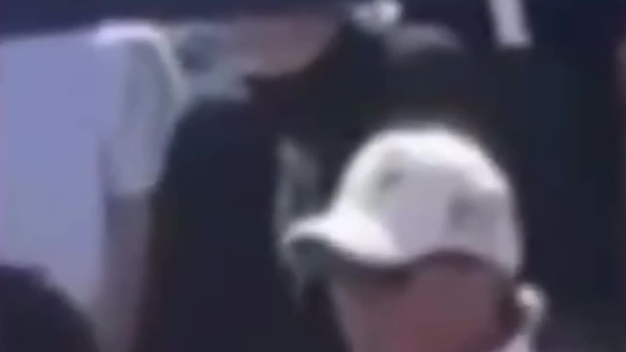 Guys in White and Black standing behind Charlie making what appears to be hand signals.