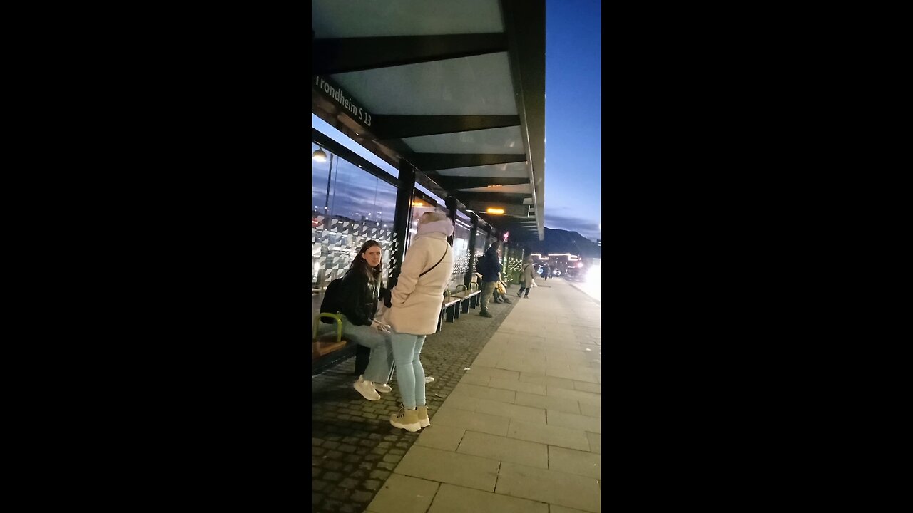 Two beautiful young girls in light jackets are freezing while waiting for the bus.