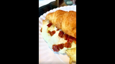A warm croissant sandwich with bacon, eggs, burrata, and pesto