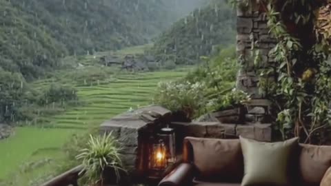 Panoramic resort balcony with raining, misty mountains, lush valley views.
