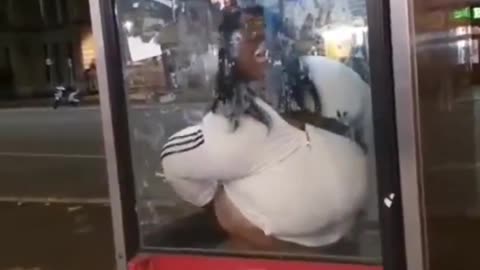 A very fat woman defecates a public telephone booth.