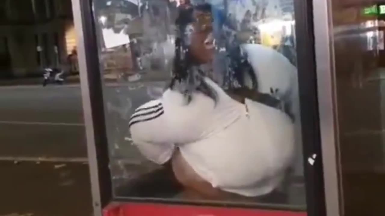 A very fat woman defecates a public telephone booth.