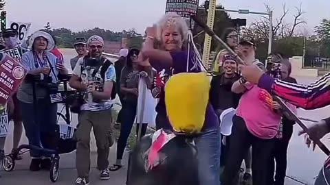Old woman wearing a "be kind" shirt tries to decapitate a Trump effigy