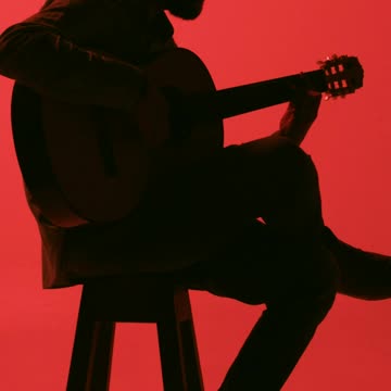 Silhouette of a guitarist playing sitting on a bench