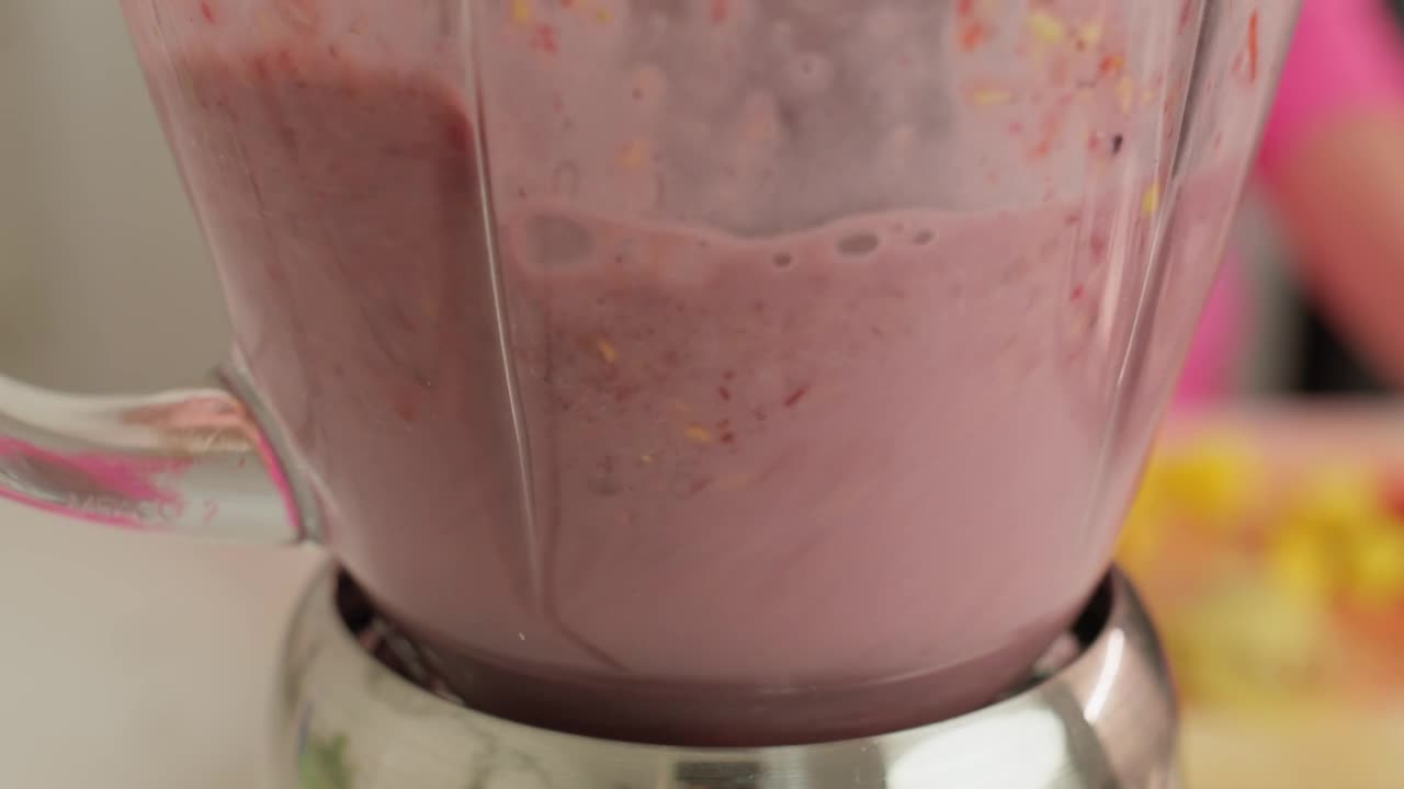 Blending a smoothie of various fruits inside a blender with milk.