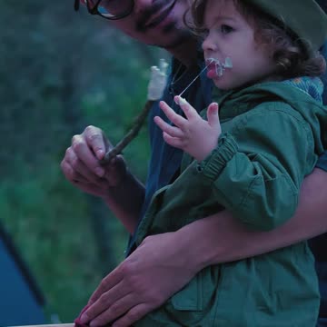Father and his little daughter eating marshmallows in nature