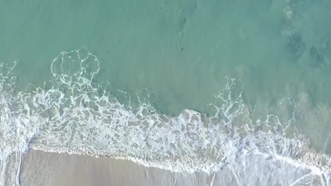 Aerial view of the beautiful turquoise waves crashing on the sand beach with white umbrellas