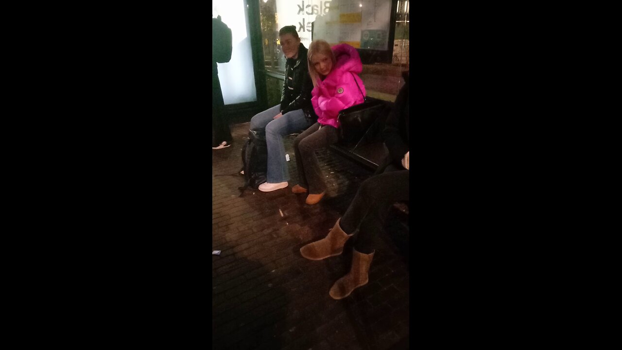 Beautiful young girl in a pink light jacket freezes while waiting for the bus.