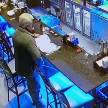 A man pretending to look at a menu at the bar while he takes a piss next to it