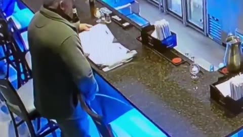 A man pretending to look at a menu at the bar while he takes a piss next to it