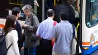 A photograph of passengers boarding a New Flyer city bus in an urban environment during daytime.