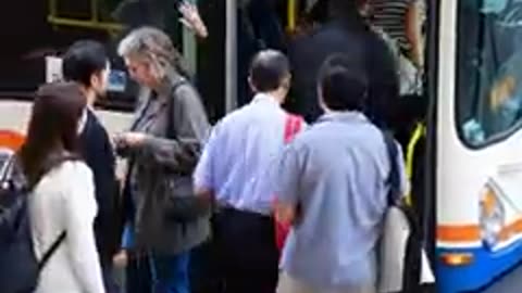 A photograph of passengers boarding a New Flyer city bus in an urban environment during daytime.