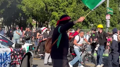 Rioter waves a Mexican Flag in front of a burning vehicle in LA