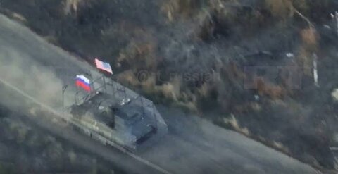 A Russian military vehicle attacks Ukrainian positions while flying the Russian and American flags