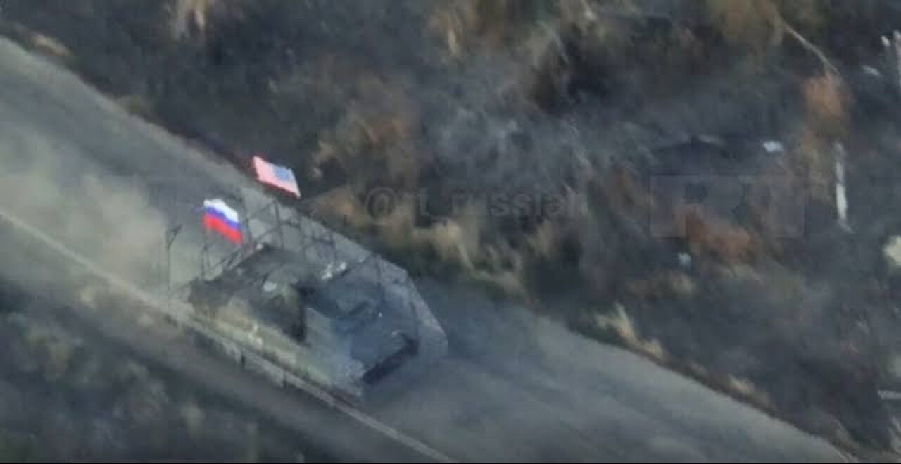 A Russian military vehicle attacks Ukrainian positions while flying the Russian and American flags