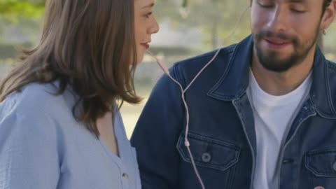 A young happy couple share a wired heaphone at the park bench