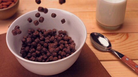 A continuous stream of chocolate flavored cereal fall into a pristine white bowl on the table