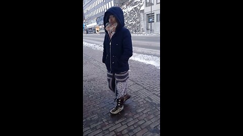 Woman in a light winter jacket freezes (short sssss.....) while waiting for a bus.