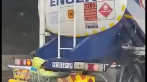 A lunatic in a shopping cart is hitched to a truck on the highway