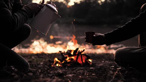 People sharing a warm drink around a camp fire in the early evening.