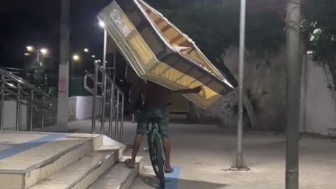 Man Carries a Bed While Riding a Bicycle