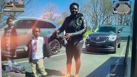 A woman approaches a Tesla with children and lifts the boy to give him a glimpse of the interior