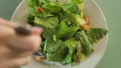 A person's hand eating healthy vegetable salad with a fork, top view.