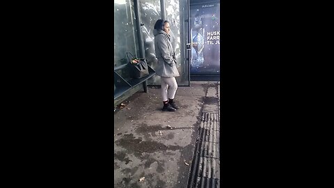 Woman in a light jacket freezes while waiting for the bus.