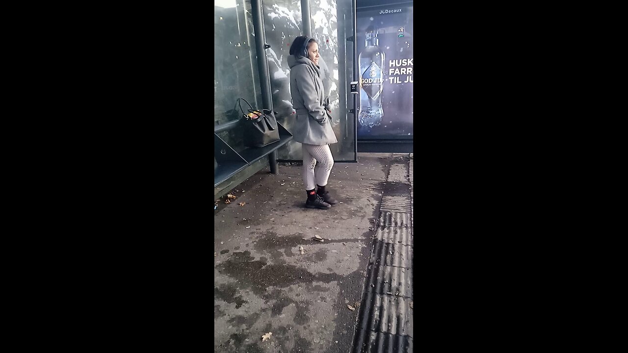 Woman in a light jacket freezes while waiting for the bus.