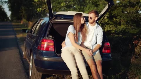Young couple kiss in back of car in sunny countryside