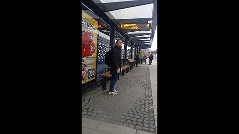 Beautiful young girl in a light jacket is freezing at real feel -4°C waiting for a bus.