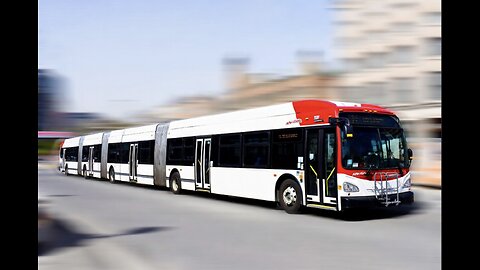 A photograph of a long New Flyer articulated city bus with multiple sections in an urban setting.