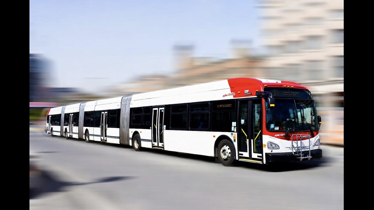 A photograph of a long New Flyer articulated city bus with multiple sections in an urban setting.